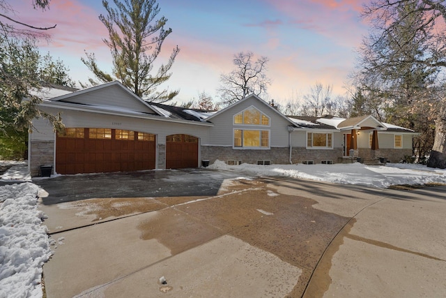 ranch-style home featuring stone siding, driveway, and a garage