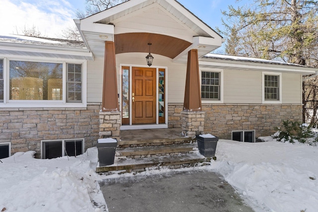 snow covered property entrance featuring stone siding