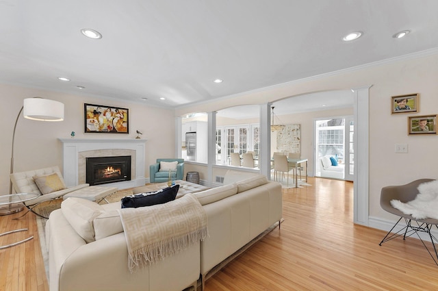 living room with decorative columns, recessed lighting, a lit fireplace, ornamental molding, and light wood-type flooring