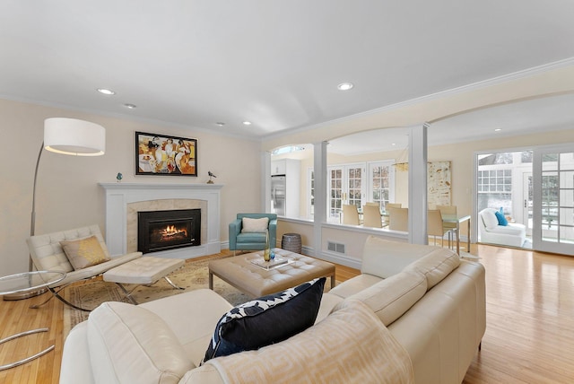 living area with visible vents, a fireplace with flush hearth, ornamental molding, decorative columns, and light wood-style floors