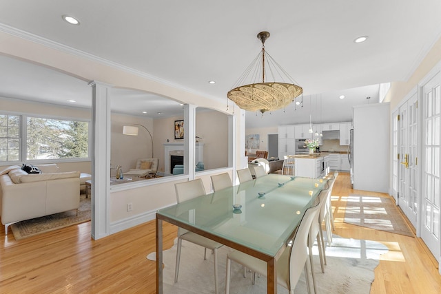 dining space featuring ornamental molding, light wood-style flooring, a fireplace, and ornate columns