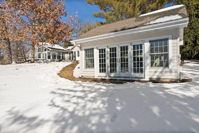 snow covered rear of property featuring french doors and a shingled roof