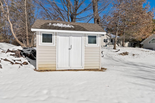 snow covered structure featuring an outbuilding and a shed