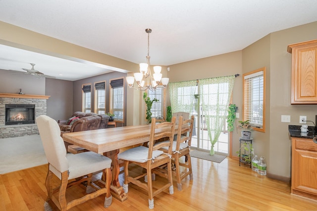 dining space with light wood-style flooring, ceiling fan with notable chandelier, baseboards, and a stone fireplace