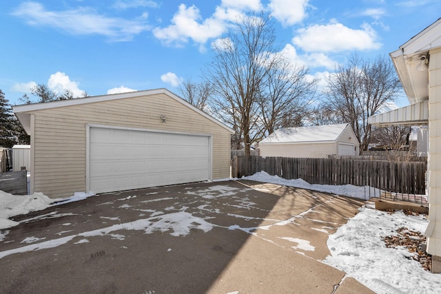 snow covered garage featuring a detached garage and fence