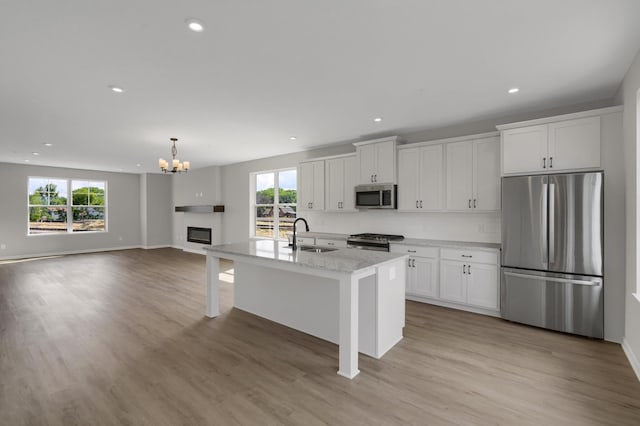 kitchen featuring white cabinetry, a sink, light wood-style floors, appliances with stainless steel finishes, and a glass covered fireplace