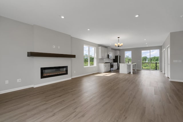 unfurnished living room with recessed lighting, baseboards, a notable chandelier, and dark wood-style floors