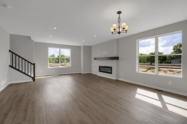 unfurnished living room with a glass covered fireplace, visible vents, stairs, and dark wood-type flooring