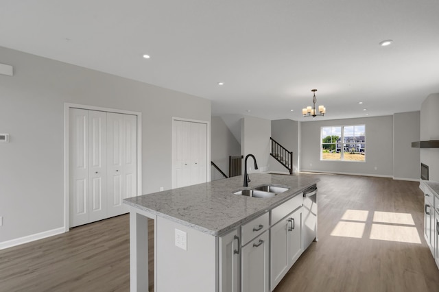 kitchen with a sink, a chandelier, a center island with sink, wood finished floors, and stainless steel dishwasher