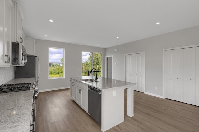 kitchen with wood finished floors, a sink, appliances with stainless steel finishes, white cabinetry, and backsplash