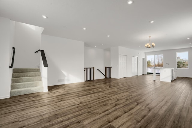 unfurnished living room with wood finished floors, recessed lighting, a sink, stairs, and a notable chandelier