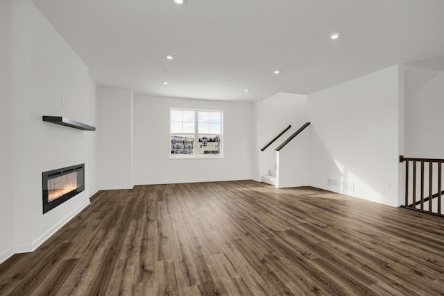 unfurnished living room featuring wood finished floors, baseboards, recessed lighting, stairs, and a glass covered fireplace