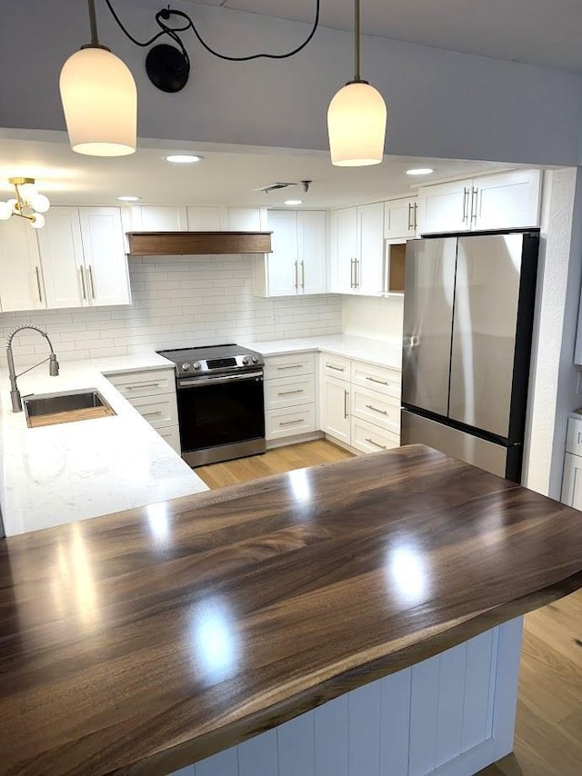 kitchen with stainless steel appliances, a sink, white cabinetry, hanging light fixtures, and decorative backsplash