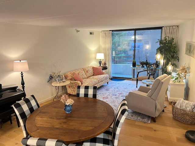 living area featuring light wood-style flooring, visible vents, a wall of windows, and baseboards