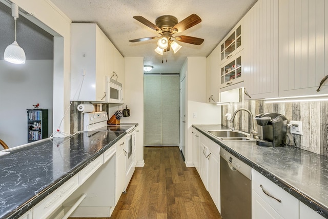 kitchen featuring white appliances, dark countertops, glass insert cabinets, pendant lighting, and a sink