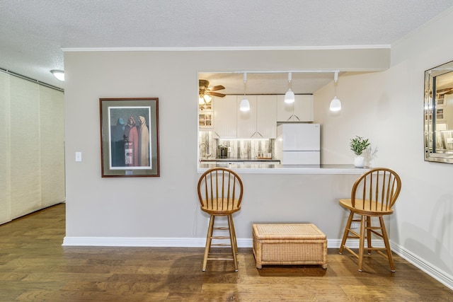 kitchen with hanging light fixtures, freestanding refrigerator, white cabinetry, a textured ceiling, and wood finished floors