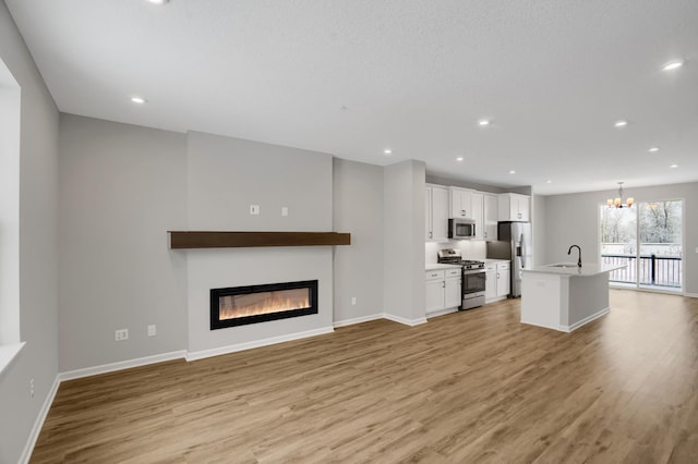 unfurnished living room featuring a chandelier, a glass covered fireplace, light wood-style flooring, and recessed lighting