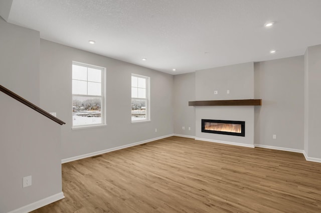 unfurnished living room featuring recessed lighting, a glass covered fireplace, a textured ceiling, wood finished floors, and baseboards