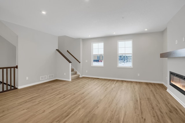 unfurnished living room with stairs, a glass covered fireplace, light wood-style flooring, and baseboards