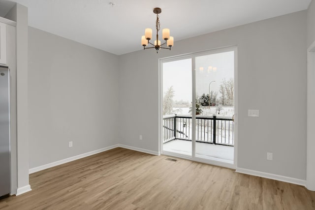 unfurnished dining area featuring baseboards, visible vents, light wood-style flooring, and an inviting chandelier