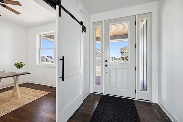 entryway with visible vents, a ceiling fan, dark wood finished floors, a barn door, and baseboards