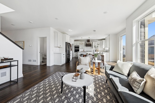 living room with stairs, visible vents, wood finished floors, and baseboards