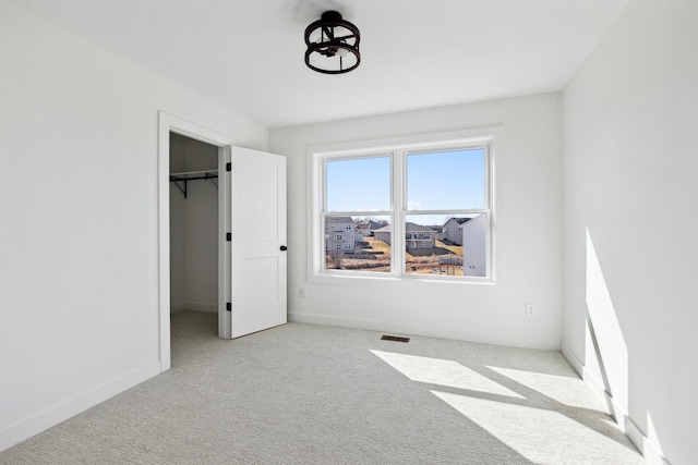 unfurnished bedroom with a spacious closet, visible vents, baseboards, carpet flooring, and a closet