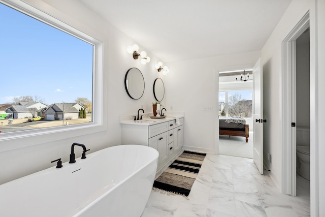 ensuite bathroom with a freestanding tub, toilet, marble finish floor, ensuite bath, and double vanity