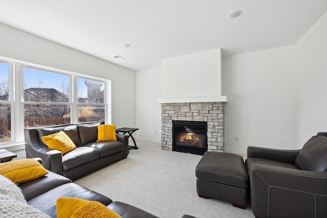 living area featuring a stone fireplace, visible vents, baseboards, and carpet