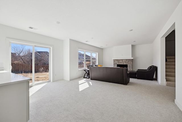 living room featuring baseboards, visible vents, a fireplace, stairs, and light carpet