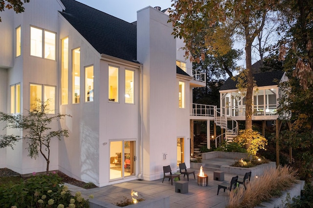 back of property with a deck, a patio, stairs, an outdoor fire pit, and a chimney