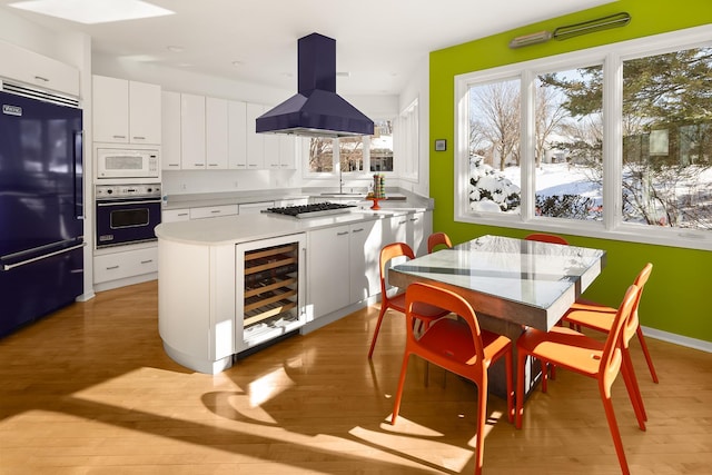 kitchen with white microwave, island exhaust hood, wine cooler, wall oven, and black fridge