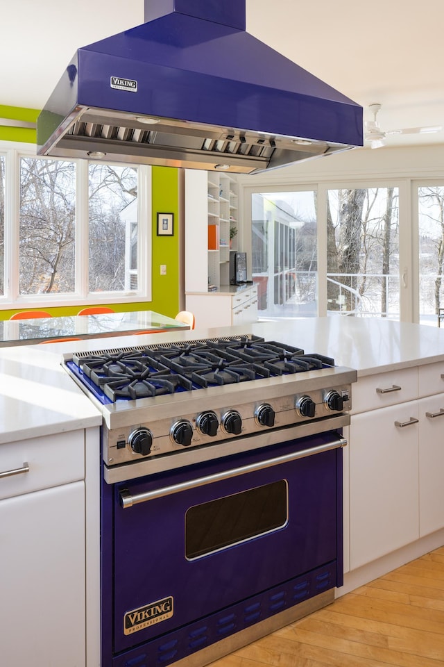 kitchen featuring range hood, premium stove, light countertops, light wood-style floors, and white cabinetry