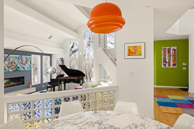 interior space featuring stairway, wood finished floors, baseboards, lofted ceiling, and a glass covered fireplace