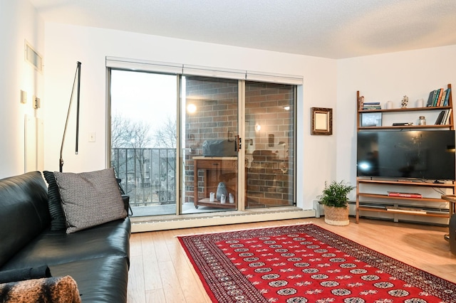 living room featuring a baseboard heating unit, a textured ceiling, wood finished floors, and visible vents