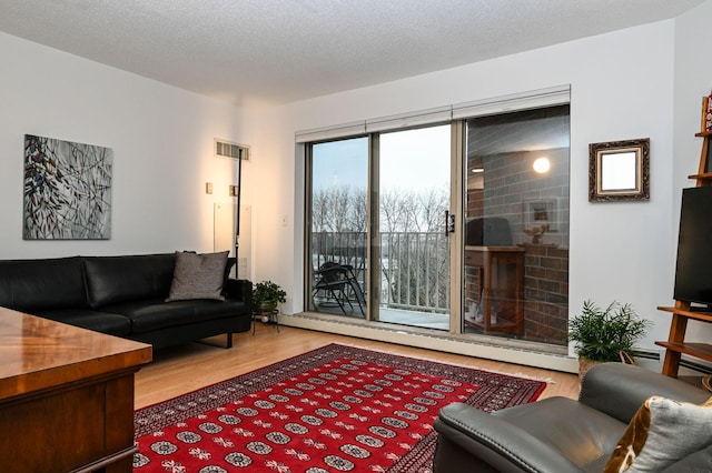 living room with a baseboard radiator, a textured ceiling, visible vents, and wood finished floors