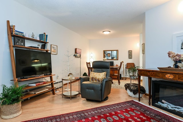 living area featuring a glass covered fireplace, baseboards, and wood finished floors