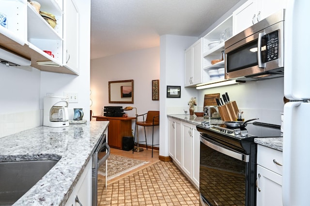 kitchen featuring appliances with stainless steel finishes, light stone countertops, white cabinetry, and open shelves