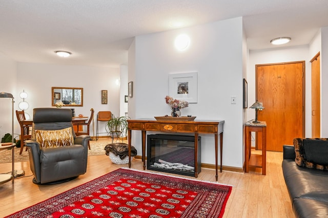 living room featuring a glass covered fireplace, baseboards, and wood-type flooring