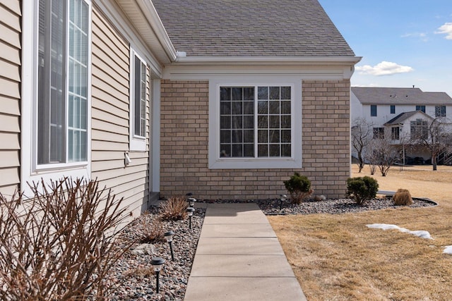 exterior space with brick siding, a lawn, and a shingled roof