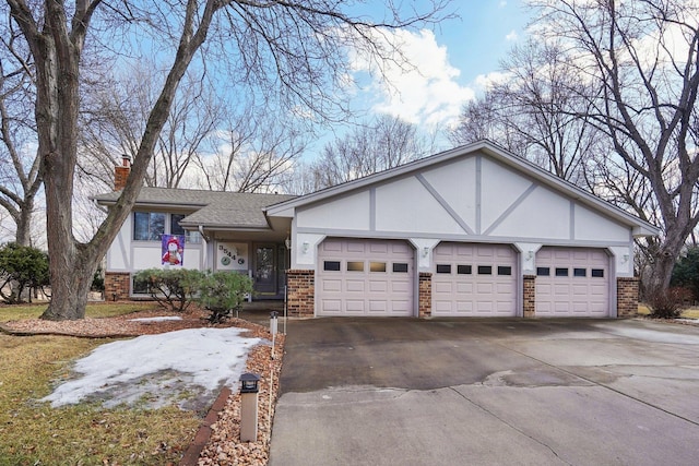 tudor-style house featuring a garage, driveway, brick siding, and a chimney