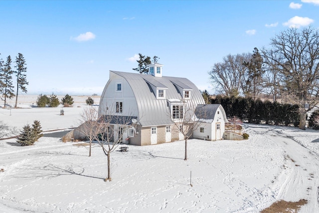 snow covered back of property with a barn, a garage, a gambrel roof, metal roof, and an outdoor structure