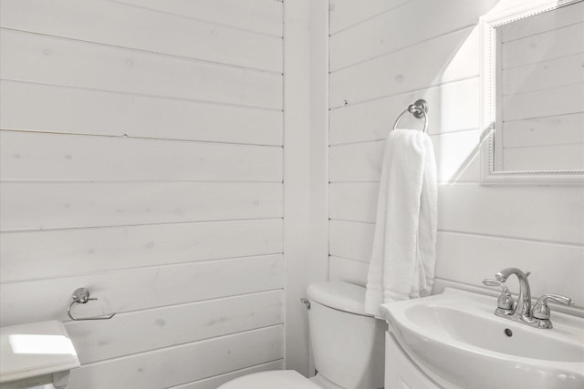 half bath featuring toilet, wood walls, and vanity