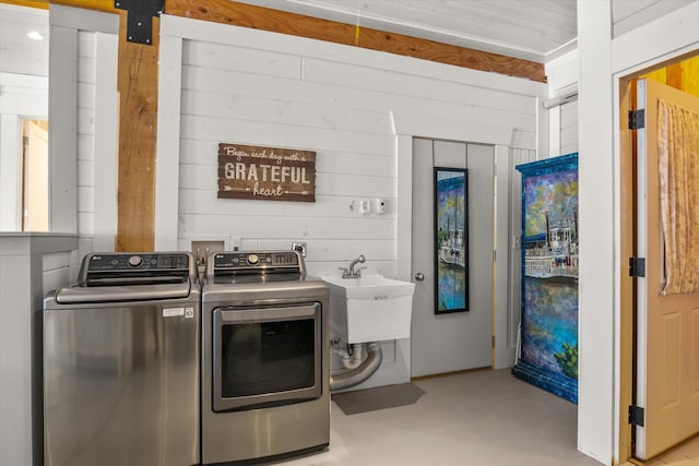 laundry area featuring wood walls, laundry area, separate washer and dryer, and a sink