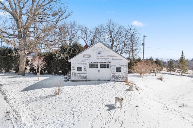 snow covered back of property featuring a detached garage and an outdoor structure