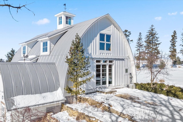 snow covered property with cooling unit, metal roof, and board and batten siding