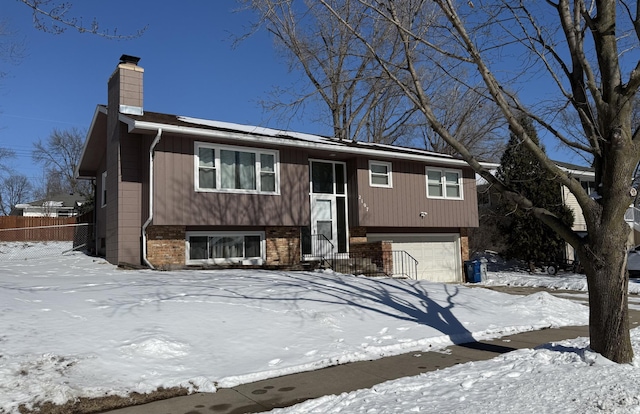 raised ranch featuring brick siding, fence, a chimney, and an attached garage