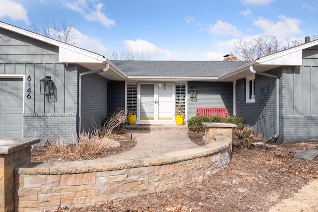 doorway to property featuring brick siding, a chimney, an attached garage, and roof with shingles