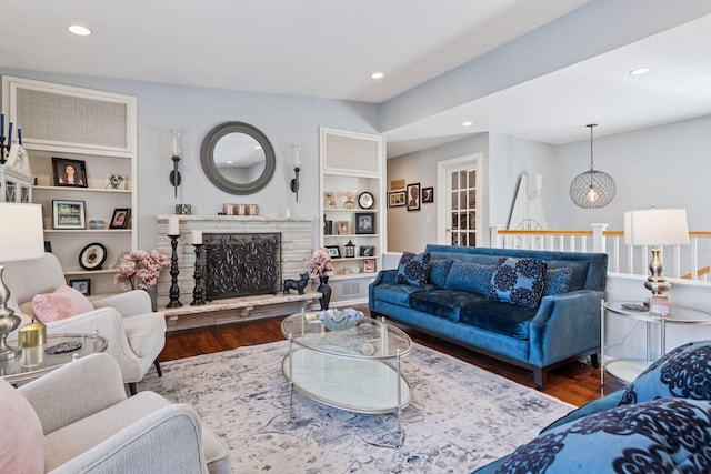 living area featuring built in features, recessed lighting, a stone fireplace, and wood finished floors