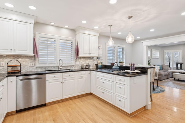 kitchen featuring a peninsula, a sink, white cabinetry, appliances with stainless steel finishes, and light wood-type flooring